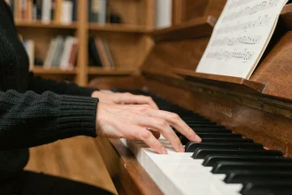 Main gauche d'une pianiste adulte jouant une note de basse en si bémol sur un piano droit, vue rapprochée sur le clavier en ambiance chaleureuse